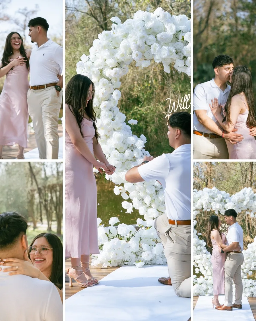 A surprise proposal under a white rose arch: he kneels with the ring, she laughs, and they kiss after she says yes. Photos by La La Vows.